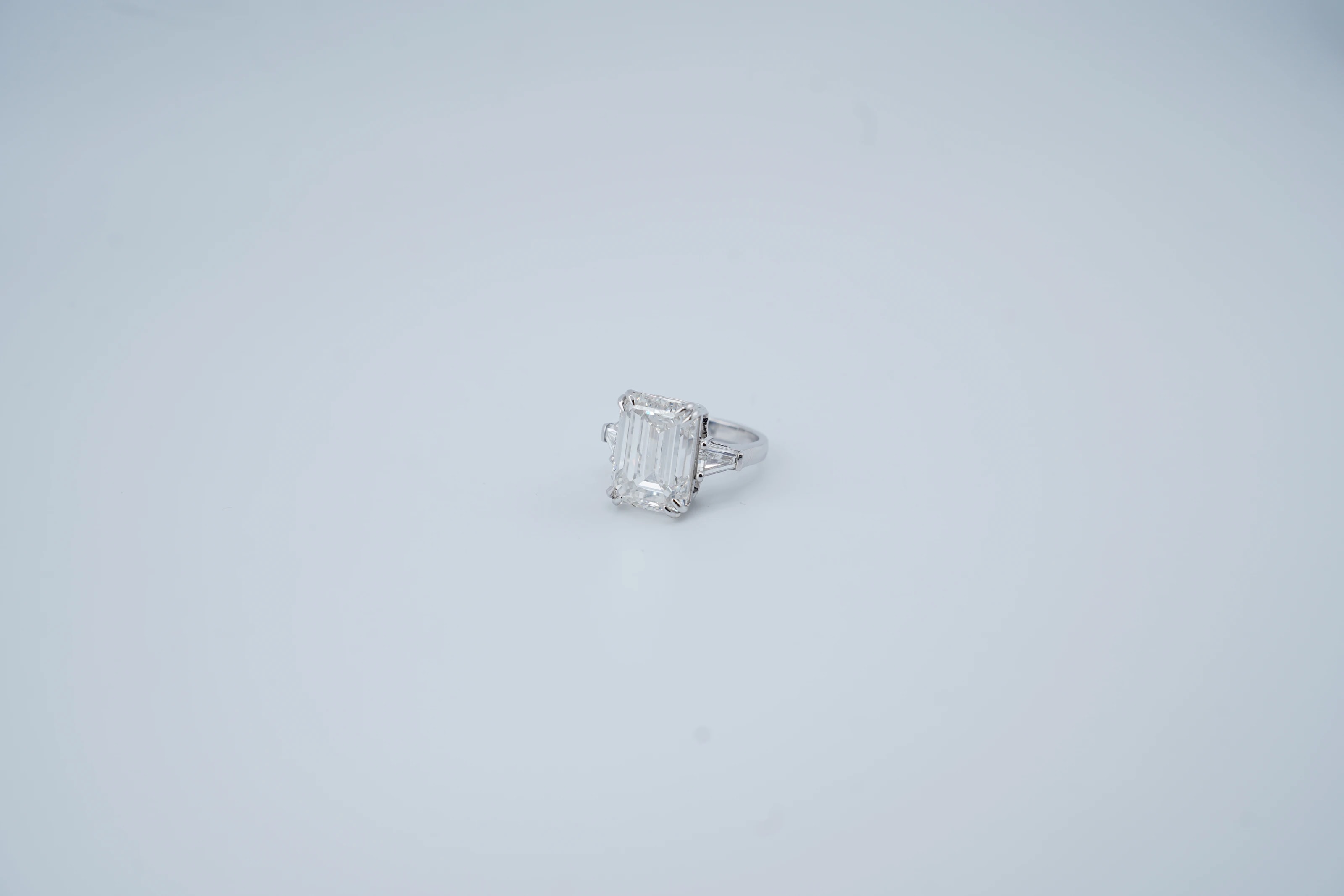 The untouched studio frame: an emerald-cut diamond ring with tapered baguettes, small on a blue-grey backdrop
