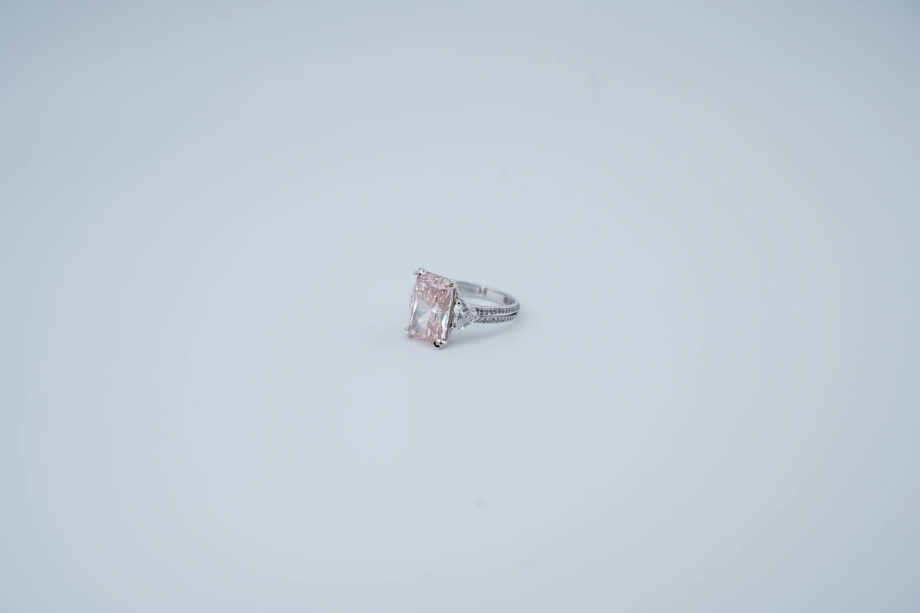 The untouched studio frame: a pink radiant-cut ring sits small and soft in the middle of a wide blue-grey backdrop